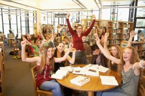 Group of teenagers with teacher cheering in library